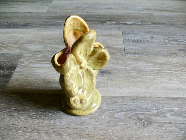 K&ouml;nnte beinhalten: Eine Vintage-Keramikvase in Form einer stilisierten Blume, mit hellgr&uuml;ner Au&szlig;enseite und rosa Innenraum. Die Vase hat eine strukturierte Oberfl&auml;che und einen abgerundeten Boden. Die bl&uuml;tenartige &Ouml;ffnung ist breit und offen.