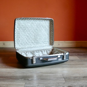May include: A vintage gray suitcase with a white floral lining. The suitcase is open and the lid is propped up.
