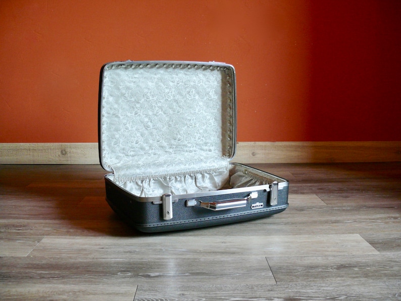 May include: A vintage gray suitcase with a white floral lining. The suitcase is open and the lid is propped up.