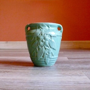 May include: A light green ceramic vase with a floral design. The vase has two small handles and a textured surface. The vase is approximately 6 inches tall and 5 inches wide, suitable for home decor.