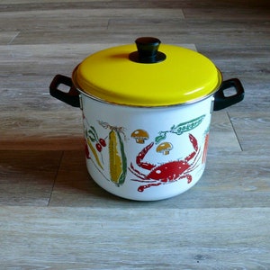 May include: A white enamel pot with a yellow lid and a black handle. The pot has a colorful design of a crab, corn, peas, and mushrooms.