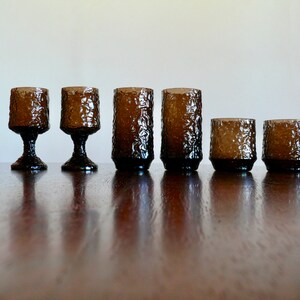 May include: Set of six brown glass tumblers with a textured surface. The tumblers are arranged in a row on a wooden surface.