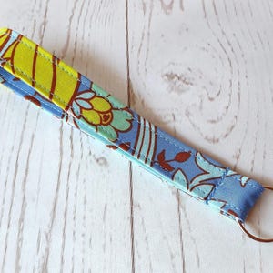 May include: A blue and yellow floral patterned fabric key chain with a silver key ring.