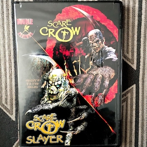 May include: A DVD case featuring a double feature of Scarecrow and Scarecrow Slayer. The cover art displays two distinct monster figures against a black and red background, with yellow text titles and a small fairy logo in the upper left corner.