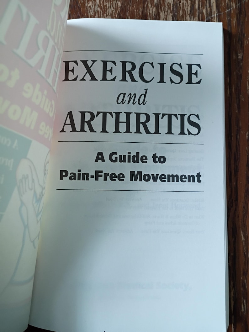 May include: An open book displaying the title "EXERCISE and ARTHRITIS" in bold black text. The subtitle reads "A Guide to Pain-Free Movement." The pages are white, and the background is a wooden surface.