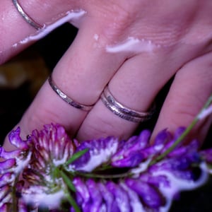 Peut inclure: Deux anneaux en argent sur un doigt, avec une fleur violette en arri&egrave;re-plan.