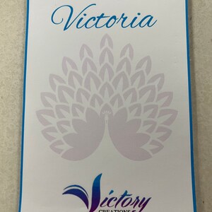 May include: A white card with a blue border. The card has a note from Victoria with a peacock design and the text "Victory Creations".