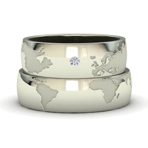 Peut inclure: Deux alliances en argent avec un motif de carte du monde. La bague du dessus a un petit diamant au centre.