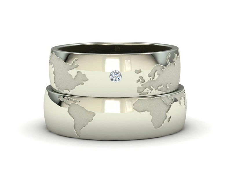 Peut inclure: Deux alliances en argent avec un motif de carte du monde. La bague du dessus a un petit diamant au centre.