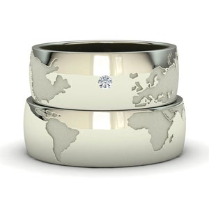 Peut inclure: Deux alliances en argent avec un motif de carte du monde. La bague du dessus a un petit diamant au centre.