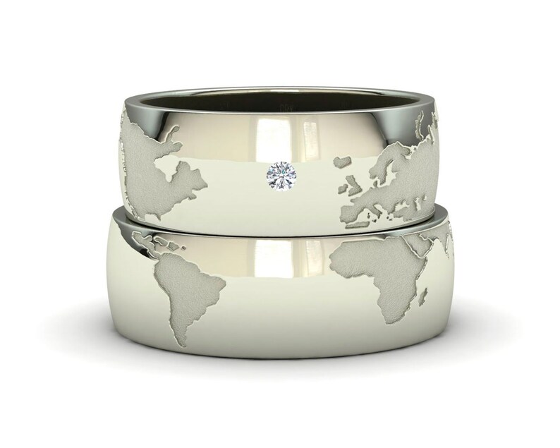 Peut inclure: Deux alliances en argent avec un motif de carte du monde. La bague du dessus a un petit diamant au centre.