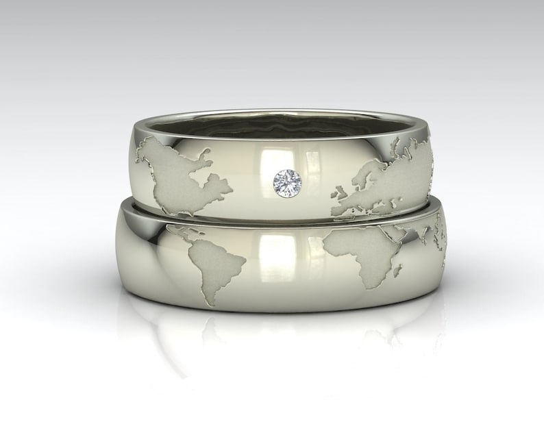 Peut inclure: Deux alliances en argent avec un motif de carte du monde. La bague du dessus a un petit diamant au centre.