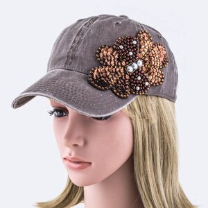 May include: A gray baseball cap with a brown and gold sequined flower embellishment.