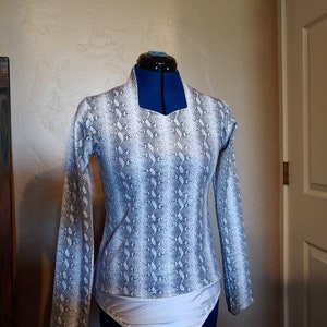 May include: A white and gray snakeskin print bodysuit with long sleeves and a scoop neck. The bodysuit has a white trim around the neckline and a white trim around the bottom.