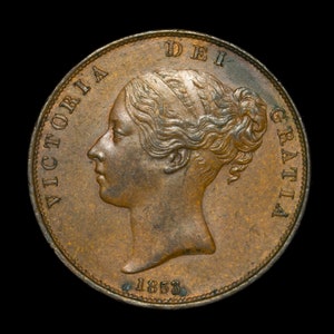 Op de afbeelding: Een koperkleurige munt met de inscriptie "VICTORIA DEI GRATIA" en het jaar "1853" rond de rand. De munt toont een profiel van koningin Victoria.