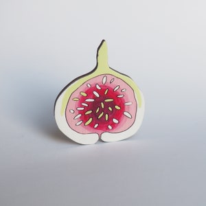 May include: A wooden fig ornament painted in shades of pink, white, and yellow. The fig is cut in half to show the inside.