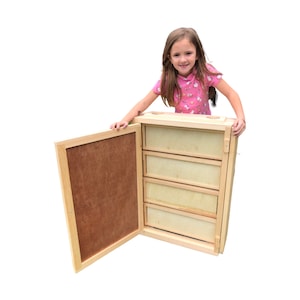 May include: A wooden cabinet with four drawers, one of which is open. The cabinet is made of light wood and has a natural finish. The drawers are made of a lighter wood and have a white finish. The cabinet is standing on a white surface.