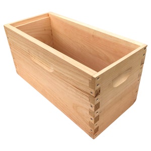 May include: A wooden beehive box with a natural finish. The box is made of pine wood and has a simple design. The box is empty and ready to be used for beekeeping.
