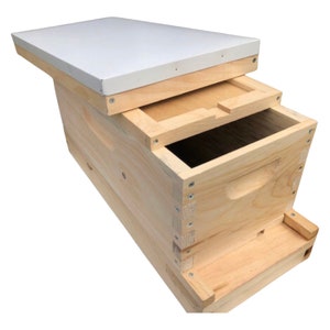 May include: A wooden beehive with a white lid. The hive is made of natural wood and has a simple design.