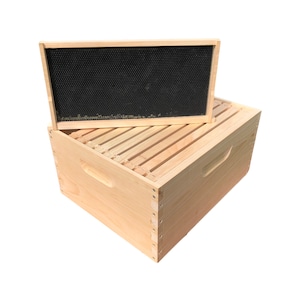 May include: A wooden beehive box with a removable frame. The frame is made of wood and has a black plastic honeycomb pattern.