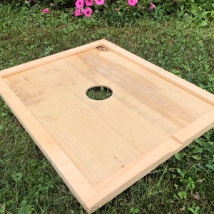 Pu&ograve; includere: Un coperchio per alveare in legno con un foro rotondo al centro. Il coperchio &egrave; in legno chiaro e ha una finitura naturale.