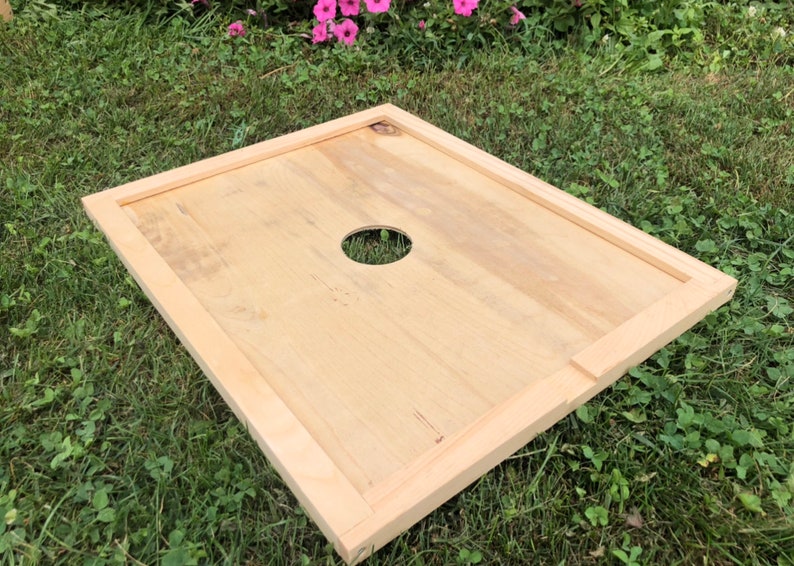Pu&ograve; includere: Un coperchio per alveare in legno con un foro rotondo al centro. Il coperchio &egrave; in legno chiaro e ha una finitura naturale.