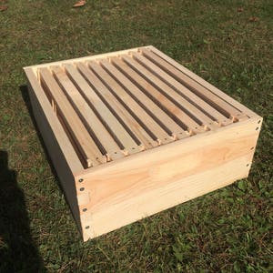 Pu&ograve; includere: Un telaio per alveare in legno con una finitura in legno chiaro. Il telaio &egrave; realizzato con sottili listelli di legno ed &egrave; progettato per contenere favi.