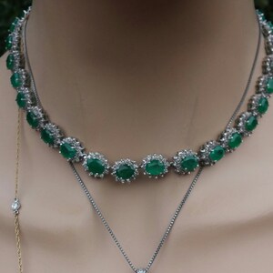 May include: A silver necklace with a row of oval-shaped green gemstones surrounded by smaller clear stones.
