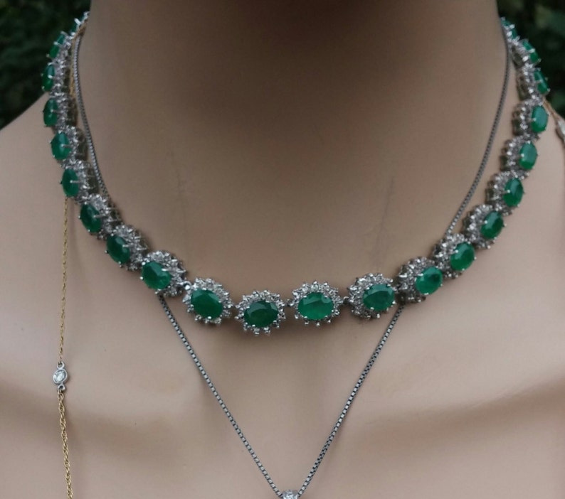 May include: A silver necklace with a row of oval-shaped green gemstones surrounded by smaller clear stones.