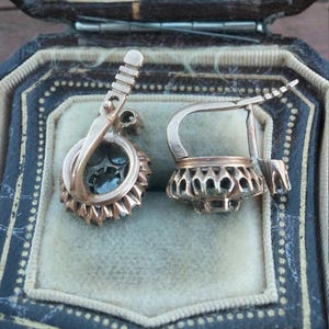May include: A pair of antique earrings with a silver filigree design and a dark blue stone in the centre. The earrings are in a velvet-lined box.