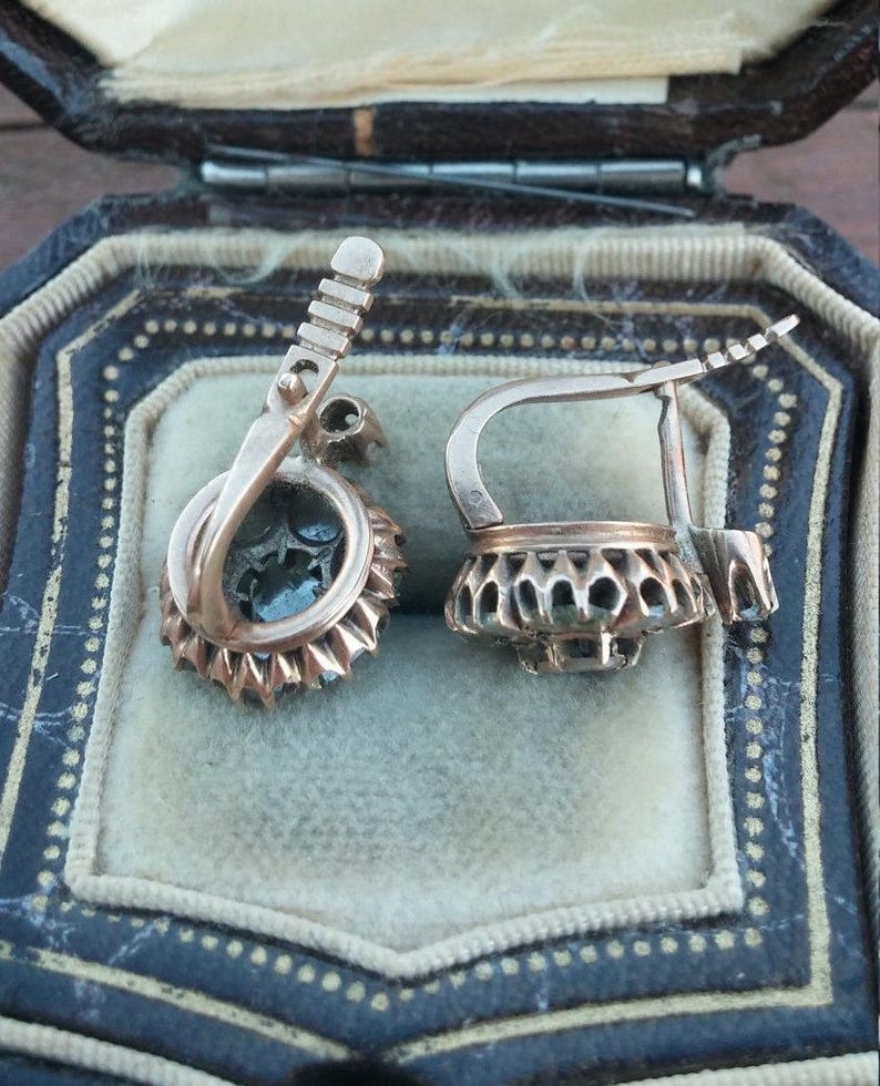 May include: A pair of antique earrings with a silver filigree design and a dark blue stone in the centre. The earrings are in a velvet-lined box.