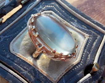 Op de afbeelding: Een vintage ring met een grote ovale, heldere edelsteen gezet in een gouden filigraan setting. De ring bevindt zich in een blauwe fluwelen ringdoos.