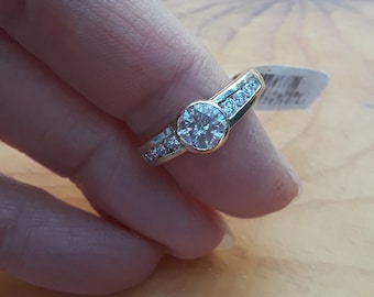 May include: A gold ring with a large round clear stone surrounded by smaller clear stones. The ring is on a finger.