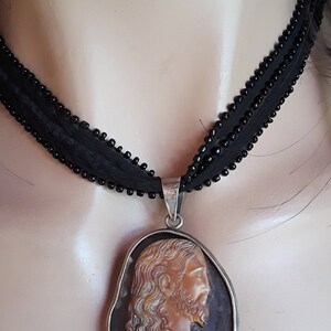 May include: A silver chain necklace with a cameo pendant featuring a carved image of Jesus Christ. The cameo is set in a silver frame and has a brown and white color scheme.