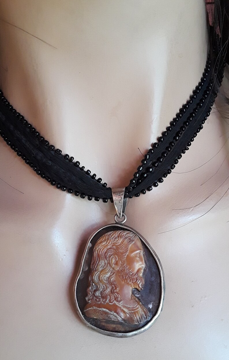 May include: A silver chain necklace with a cameo pendant featuring a carved image of Jesus Christ. The cameo is set in a silver frame and has a brown and white color scheme.