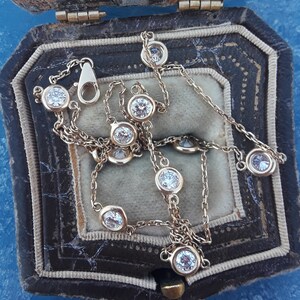 May include: A gold chain necklace with a series of round, clear gemstones. The necklace is displayed in a brown velvet jewelry box.
