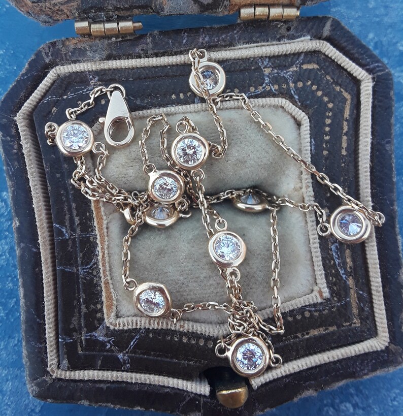 May include: A gold chain necklace with a series of round, clear gemstones. The necklace is displayed in a brown velvet jewelry box.