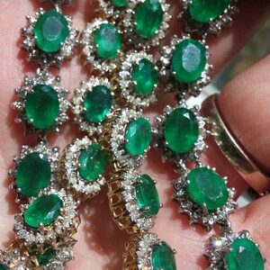 May include: A close-up of a delicate emerald and diamond necklace. The necklace features oval-shaped emeralds set in a halo of sparkling diamonds. The emeralds are a vibrant green color and the diamonds are clear and brilliant.