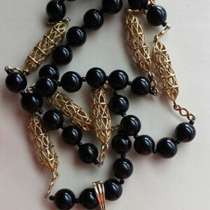 May include: A black and gold necklace with a large black oval pendant. The pendant is set with small clear stones and has a gold filigree design.