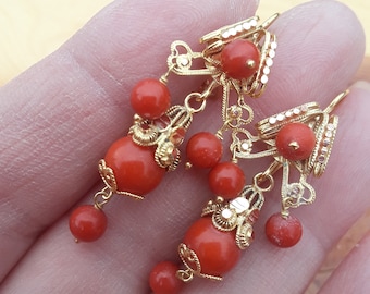May include: A pair of gold earrings with red coral beads and intricate filigree designs. The earrings have a dangling drop design with multiple coral beads.