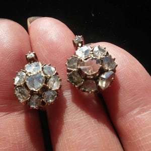 May include: A pair of antique silver earrings featuring a cluster of faceted clear stones. The stones are set in a circular pattern and have a slightly irregular shape.