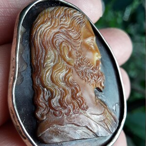 May include: A silver pendant with a cameo of a man's face carved from a brown shell. The cameo is set in a silver frame.