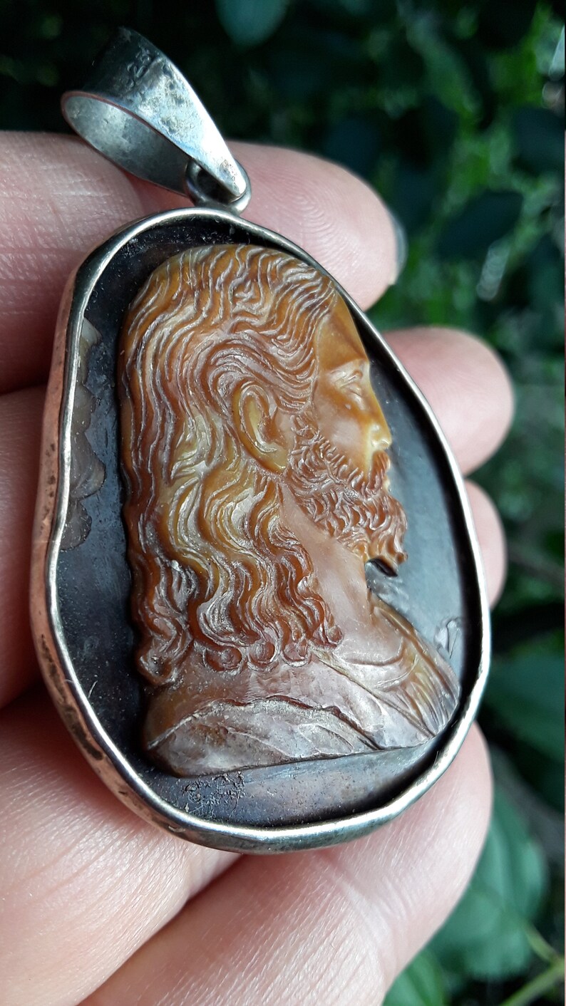 May include: A silver pendant with a cameo of a man's face carved from a brown shell. The cameo is set in a silver frame.