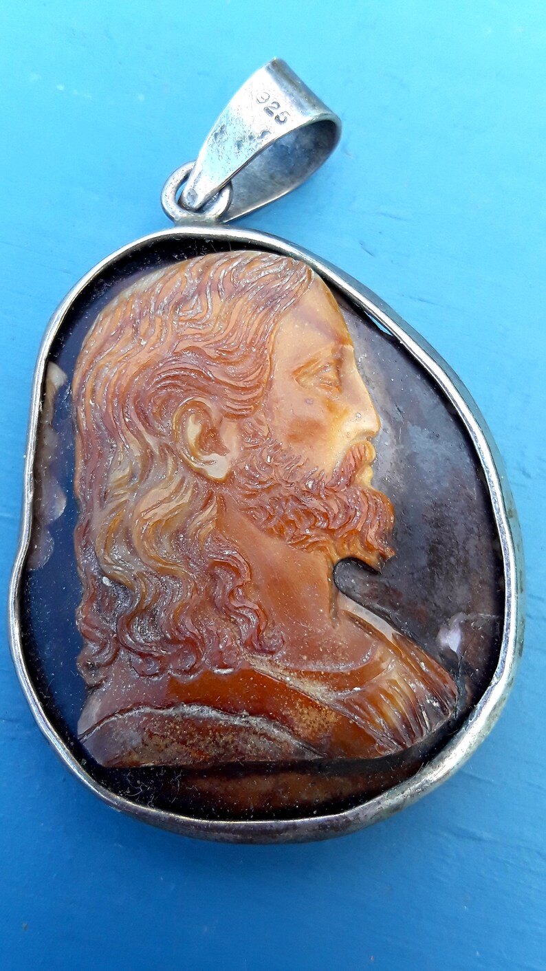 May include: A silver pendant with a cameo of a man's face carved from amber. The cameo is set in a silver frame and the pendant has a silver bail.