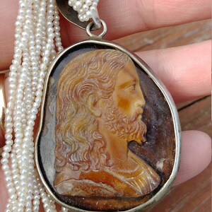 May include: A silver chain necklace with a cameo pendant featuring a carved profile of Jesus Christ. The cameo is set in a silver oval frame and is surrounded by a strand of white pearls.