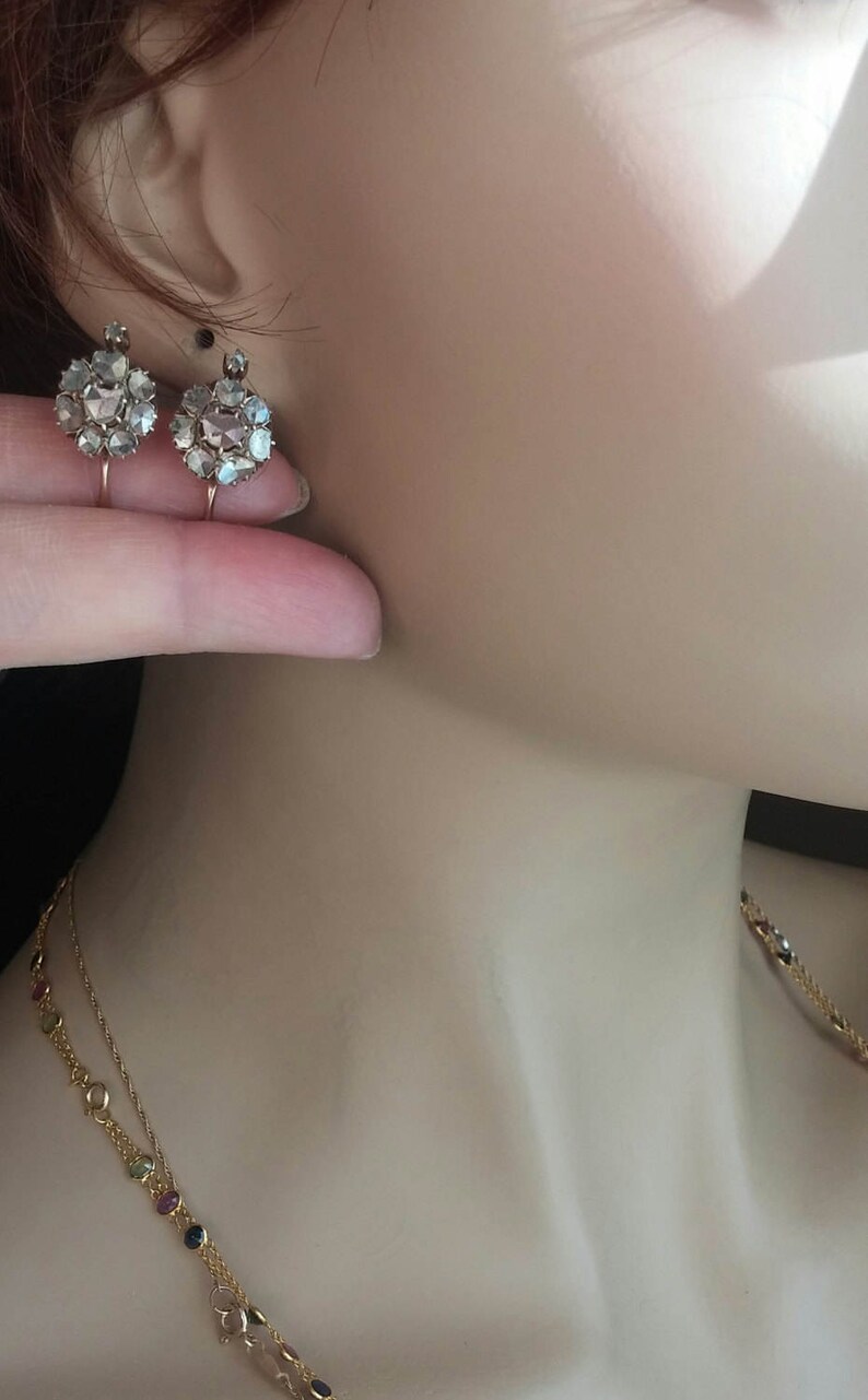 May include: A pair of antique gold earrings with a cluster of rose cut diamonds. The earrings are on a mannequin's ear.