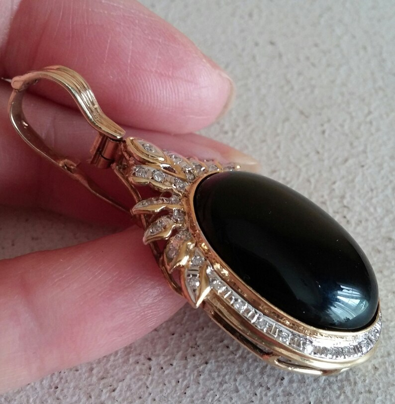 May include: A gold pendant with a black oval gemstone surrounded by a halo of small diamonds. The pendant has a bail for attaching to a chain.