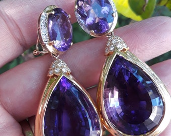 May include: A pair of gold earrings with large, pear-shaped amethyst gemstones and smaller round amethyst stones surrounded by diamonds.