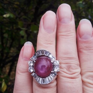 May include: A ring with a large, oval-shaped pink gemstone surrounded by smaller diamonds. The ring is set in a silver band.
