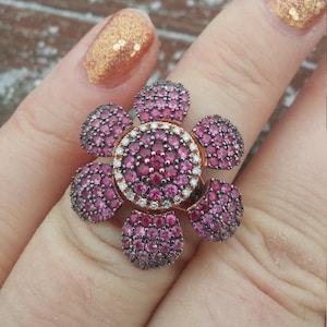May include: A rose gold ring with a flower design. The flower is made of small pink gemstones and has a center of smaller white gemstones.